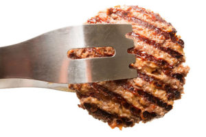 Fresh grilled beef hamburger patty held by tongs isolated on white